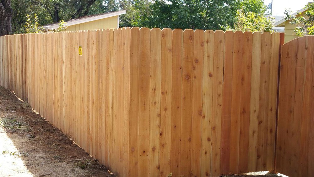 A wooden fence is sitting on top of a dirt hill next to a house