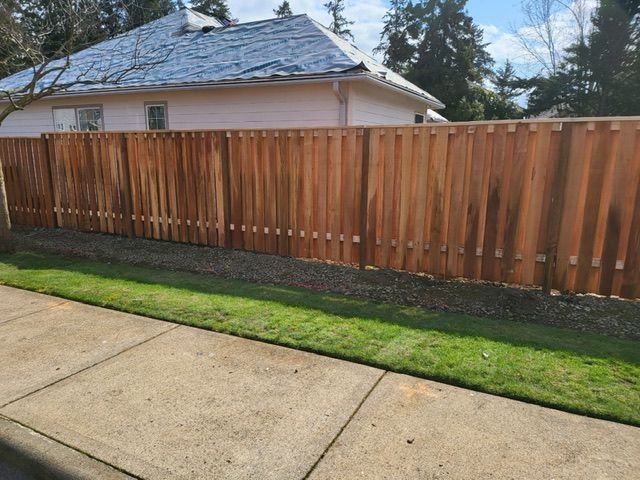 A wooden fence surrounds a lush green yard in front of a house