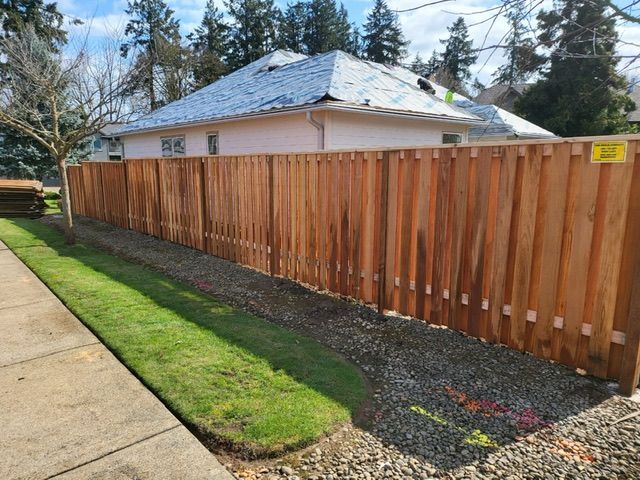 A wooden fence is sitting next to a sidewalk in front of a house