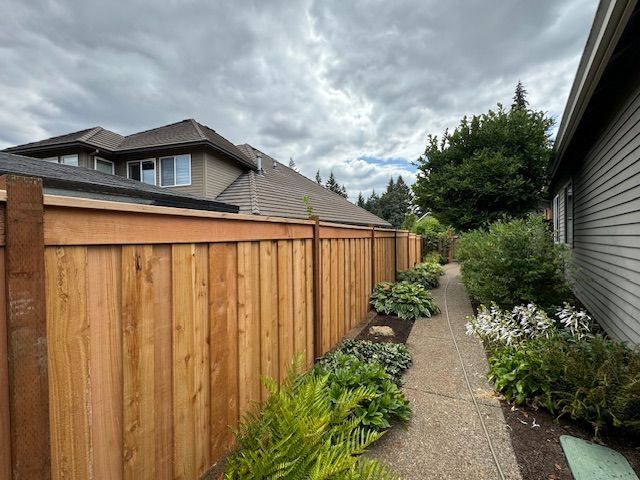 A wooden fence surrounds a sidewalk leading to a house