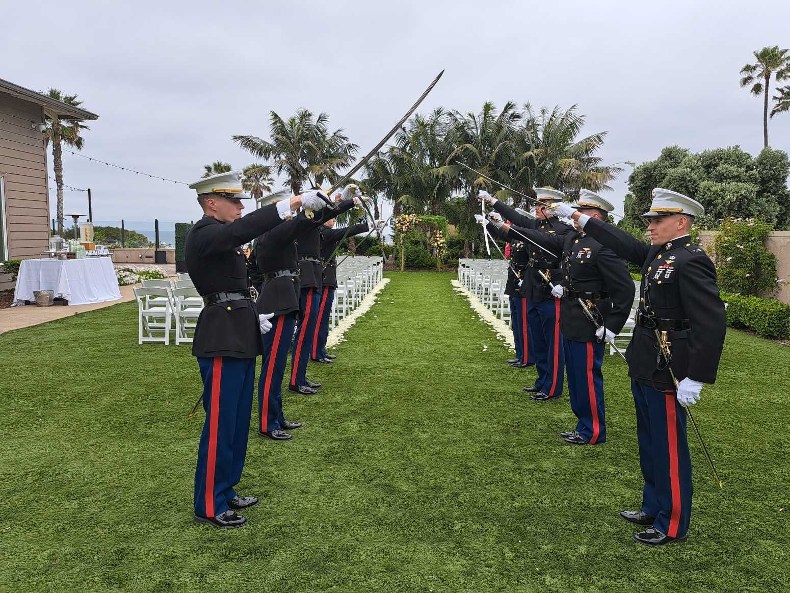 A group of men in military uniforms are standing in a grassy field holding swords.