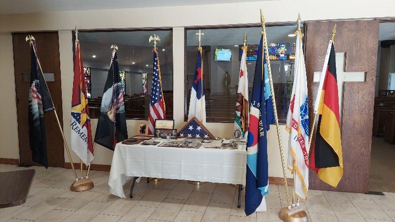 A table with flags on it in a room with a cross in the background.
