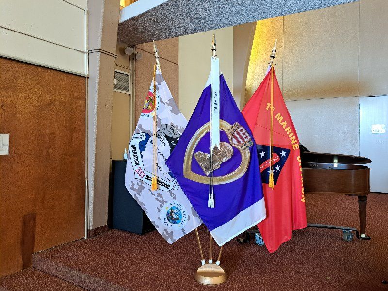 Three flags are hanging on a pole in a room with a piano.