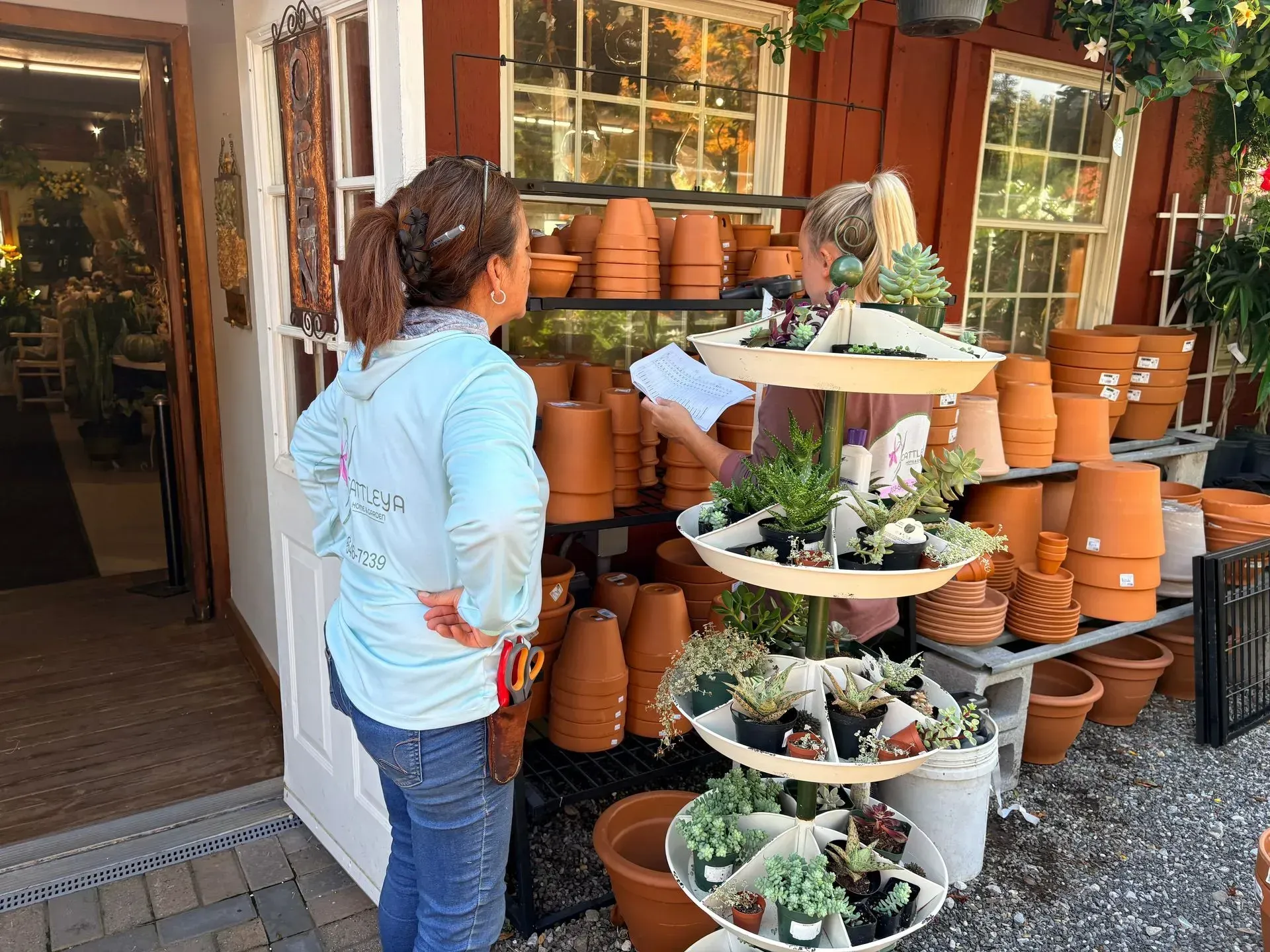 Person browsing terracotta pots and potted plants outside a garden shop.