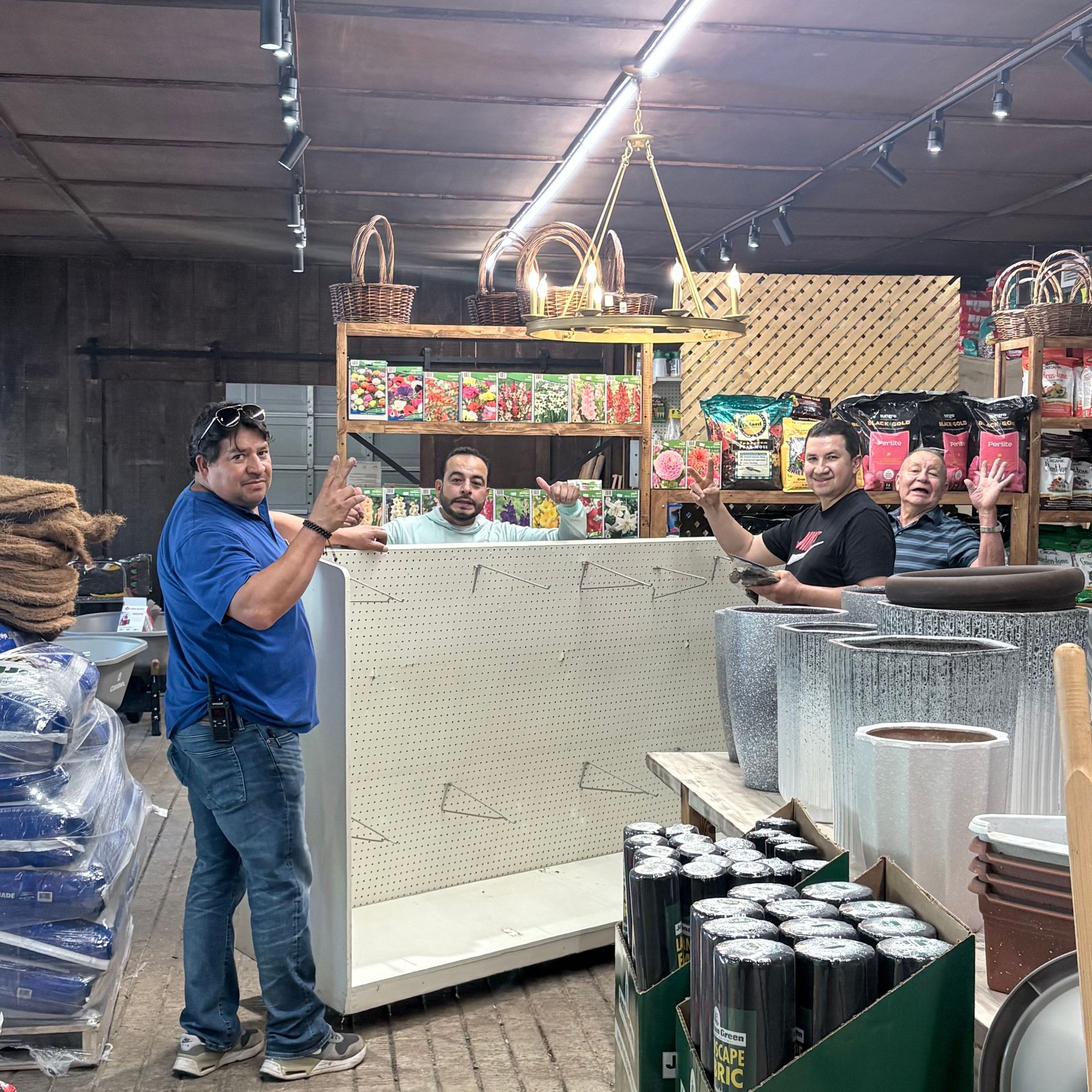 Three people smiling behind a shop counter in an industrial store aisle with shelves of colorful products.