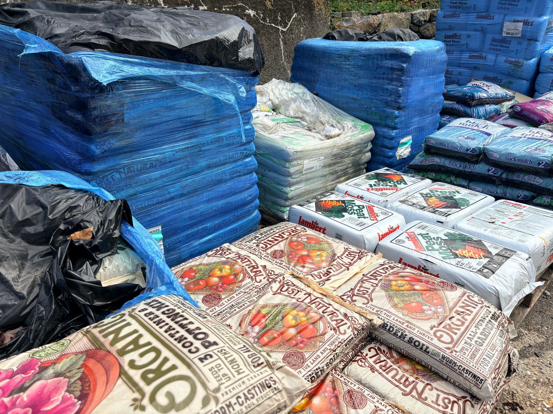 Stacks of blue and clear bagged goods and sacks with printed labels in an outdoor storage area