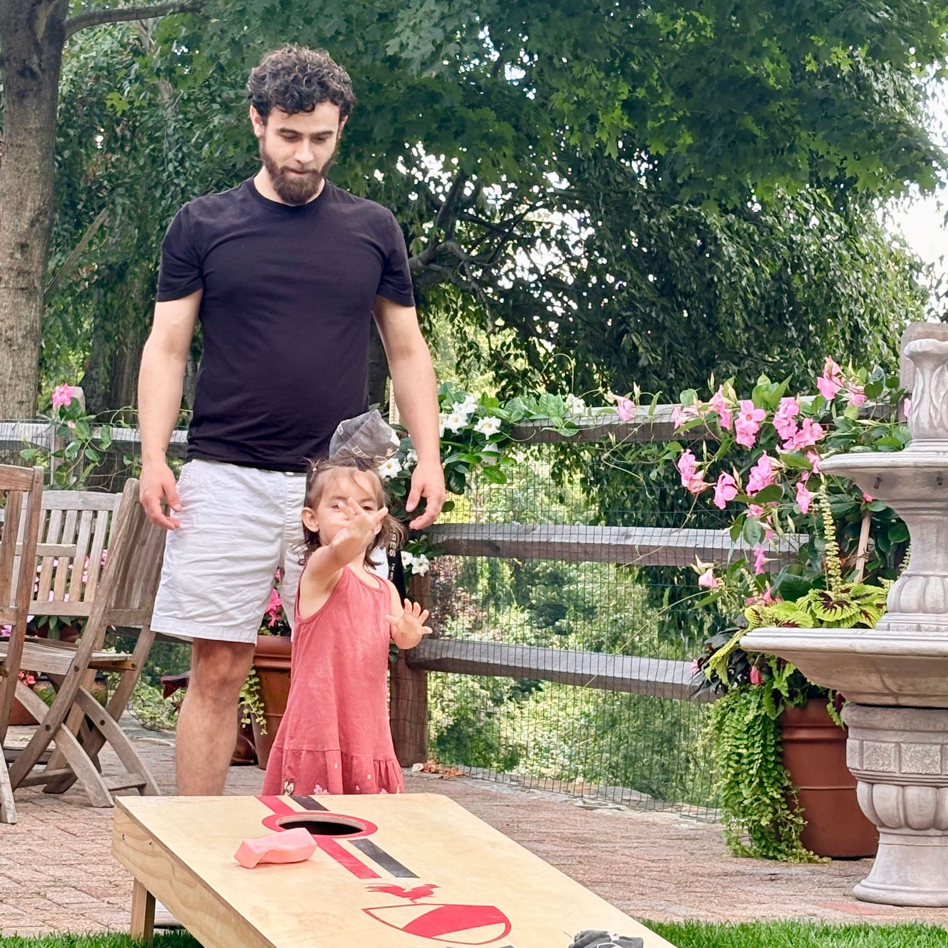 Man and child standing outdoors by a table with a large wooden number 7, surrounded by flowers and greenery