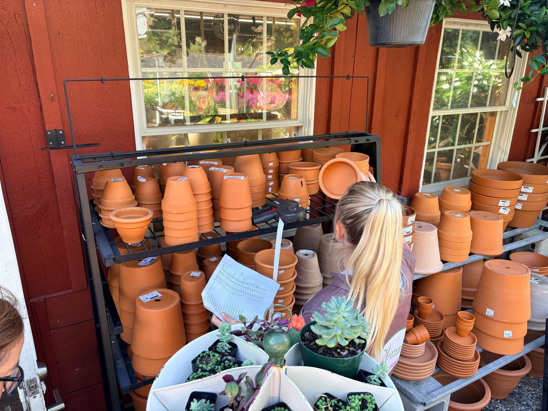 Person browsing terracotta pots on shelves outside a red wooden shop