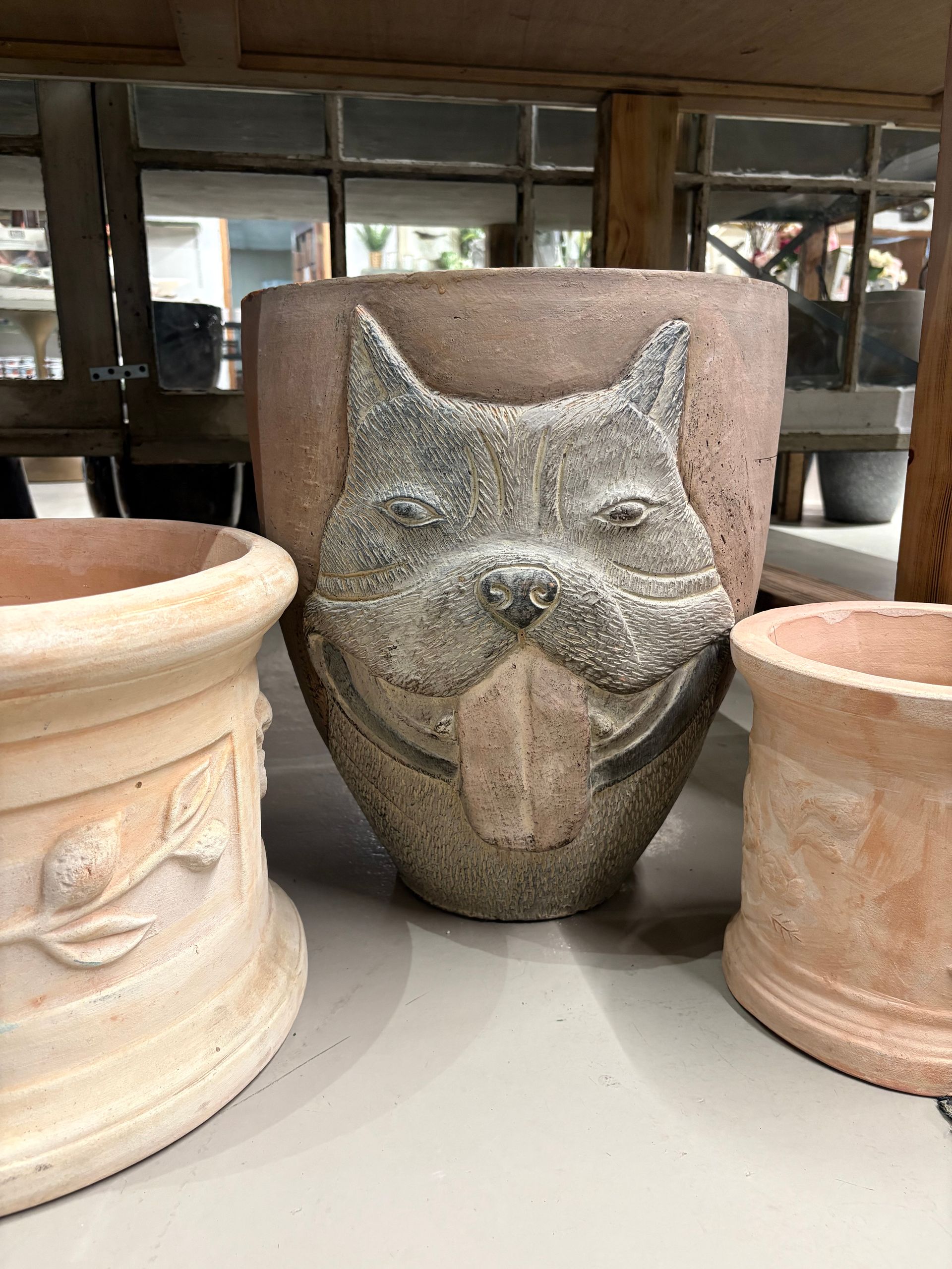 Cat-face planter between two beige terracotta pots on a shelf