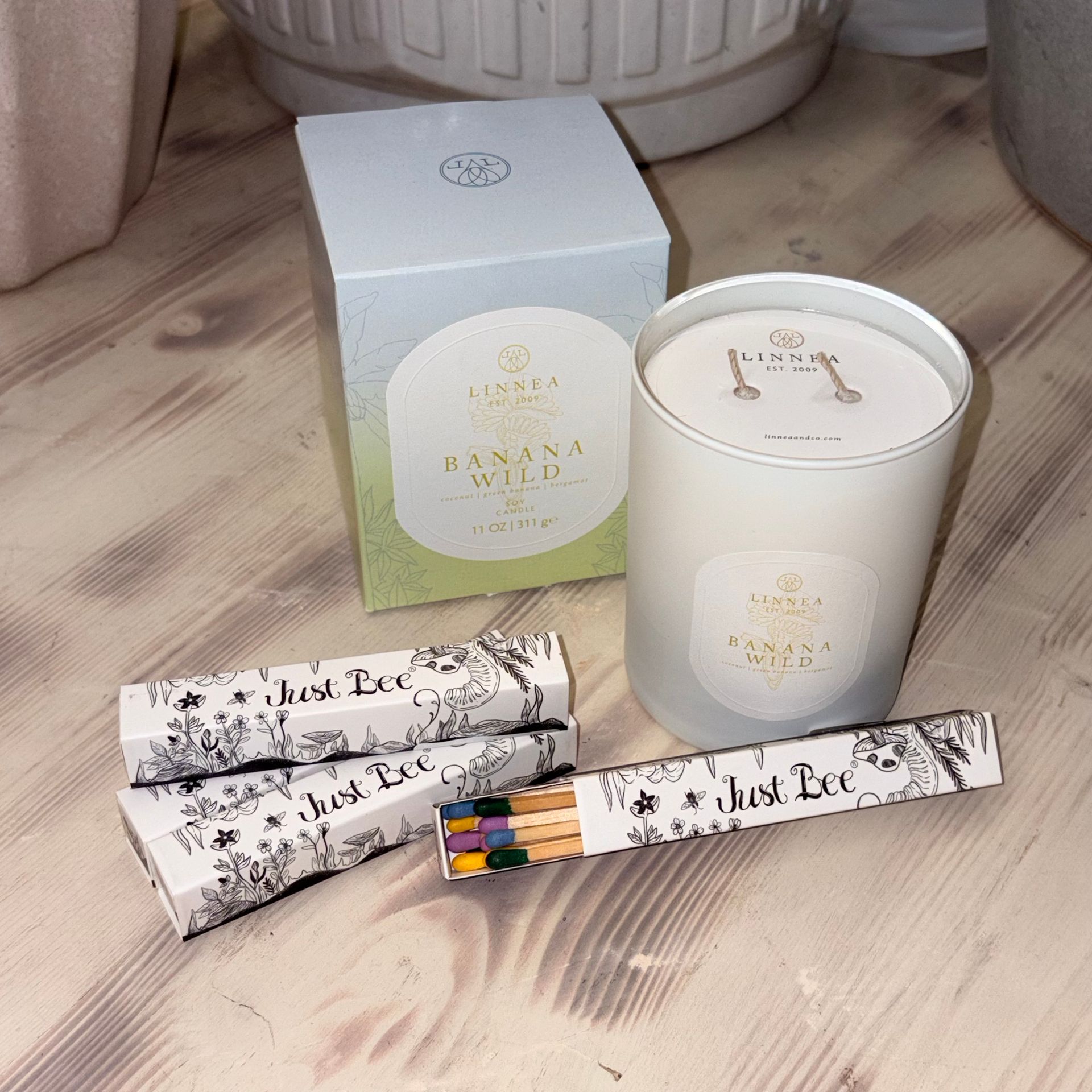 White gift box and candle beside two marble-patterned pencils on a wooden floor.