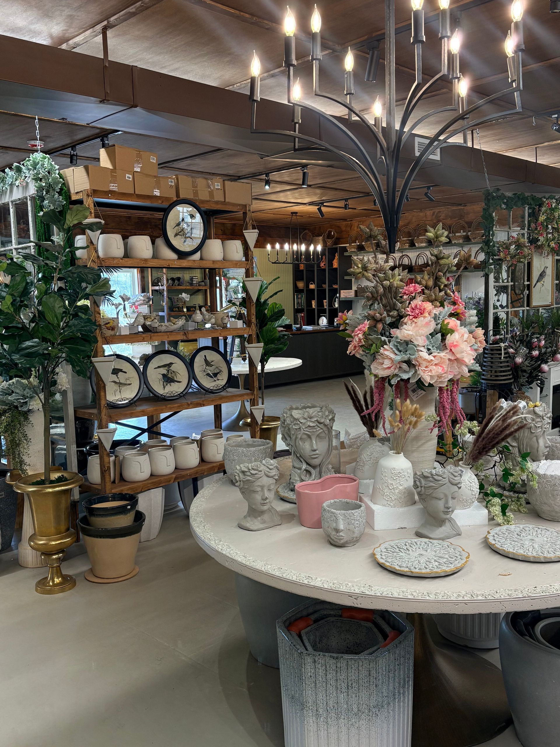 Decorative home decor display with floral centerpieces, clocks, shelves, and assorted tableware in a shop.