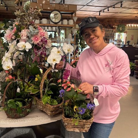 Woman in pink hoodie smiling beside baskets of orchids in a flower shop