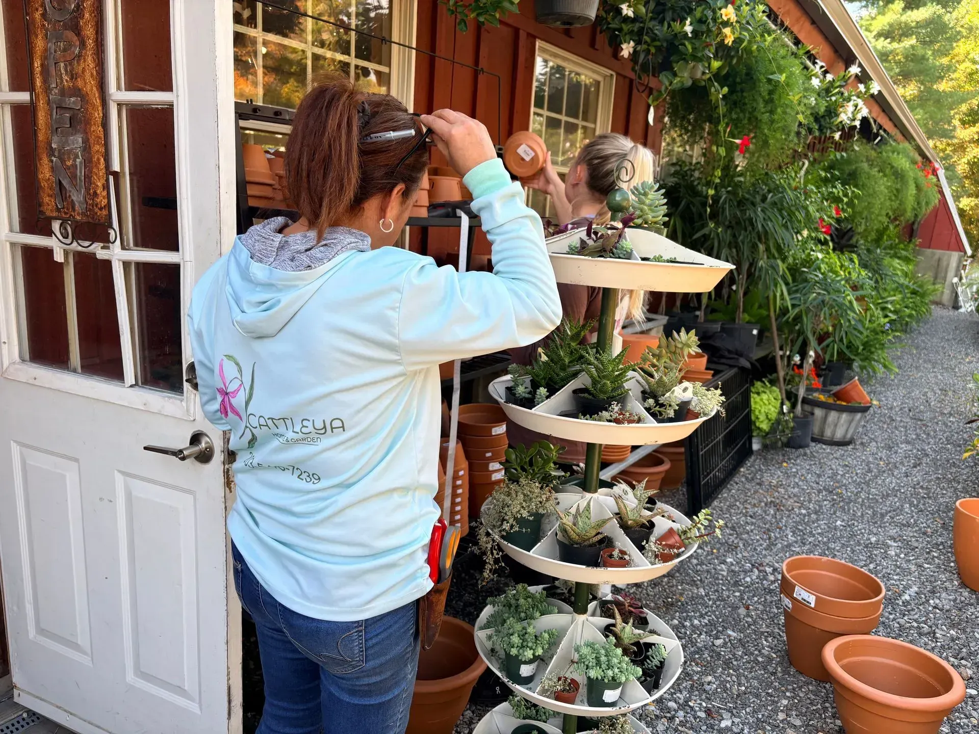 Person checking plants outside a flower shop, with hanging greenery and terracotta pots nearby.