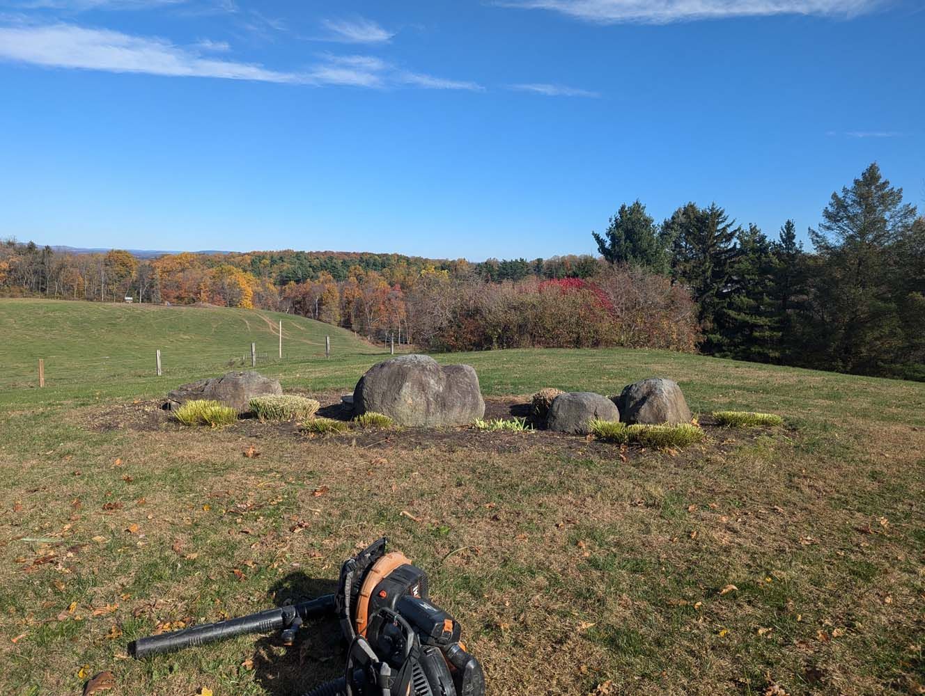 A sunny landscape with a rock garden in the foreground, fall foliage in the distance, and blue sky above.