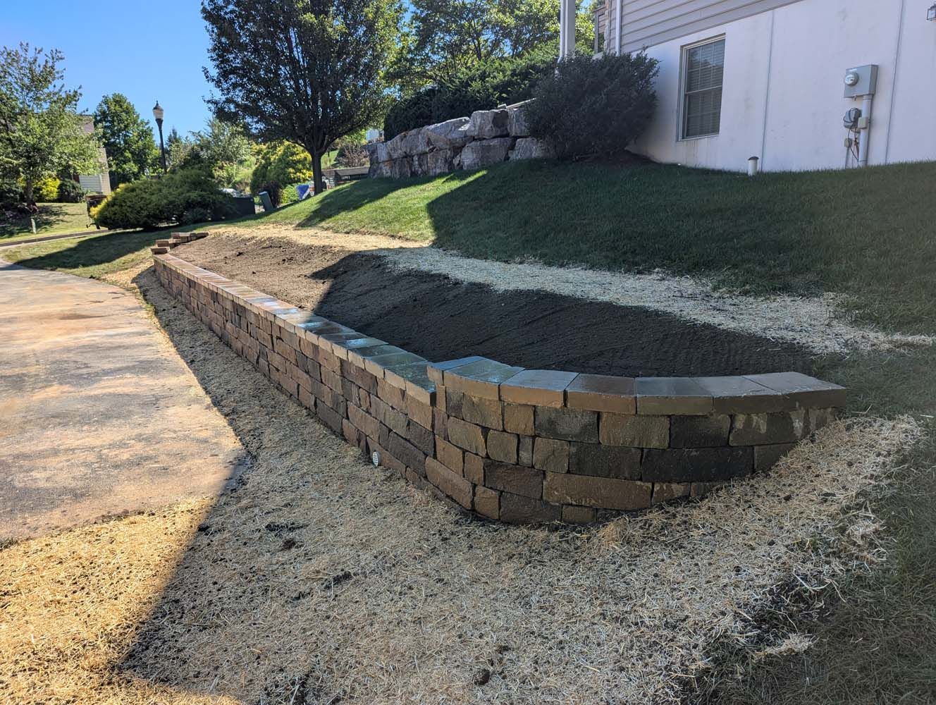 Brick retaining wall with gravel base, holding dirt and grass in front of a house.