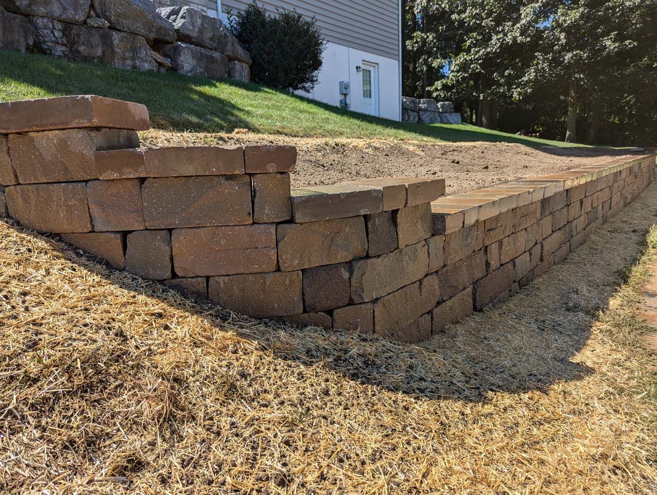 Brown brick retaining wall on a grassy slope next to a building.