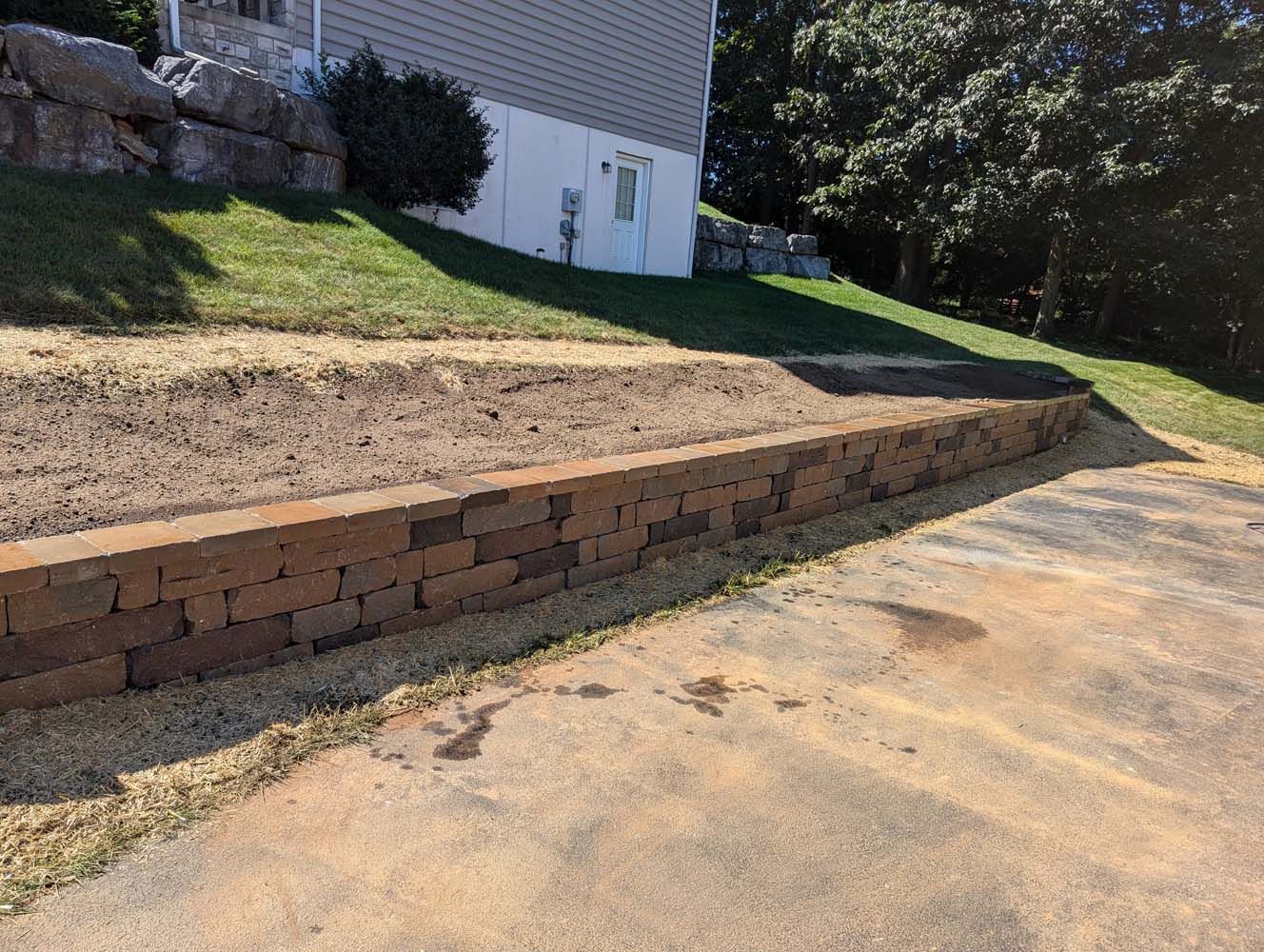 Brick retaining wall along a driveway; sloped, grassy yard above.