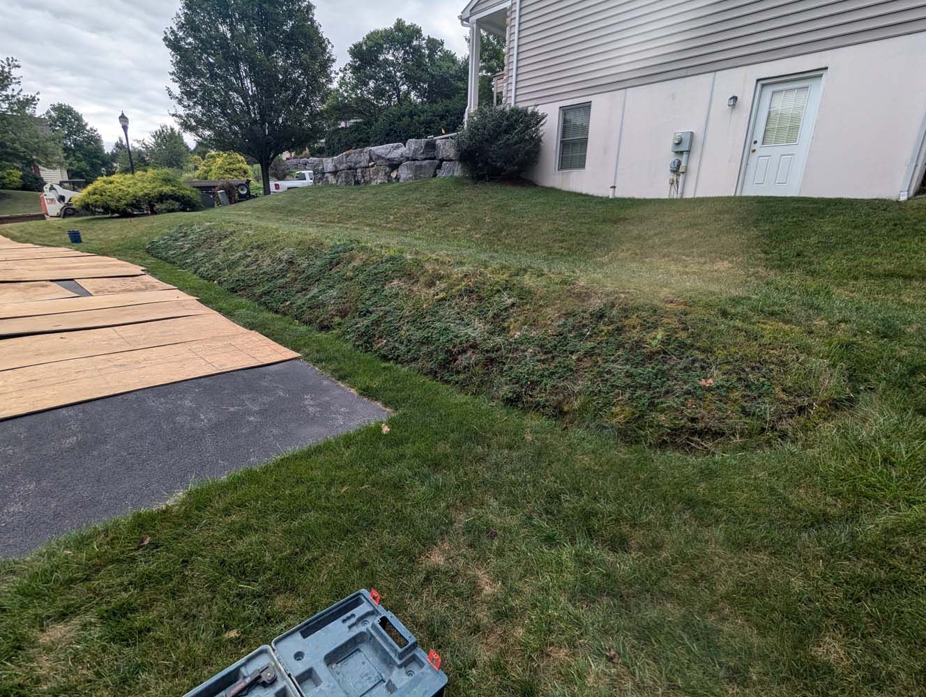 Grassy backyard with a slope, beige building, and driveway.