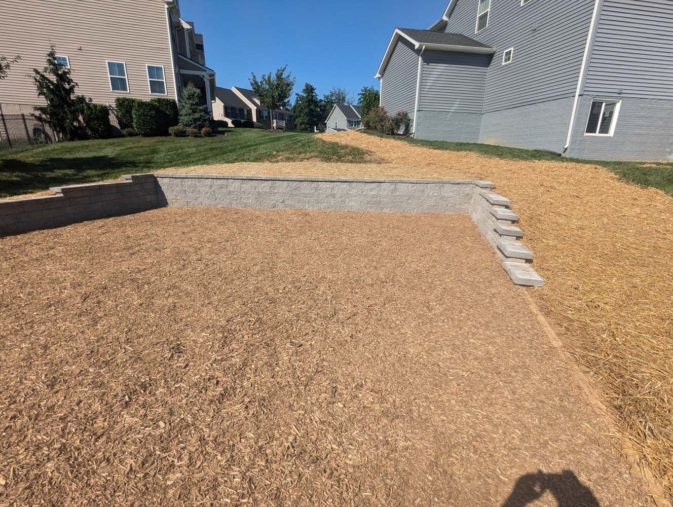 Brown mulch ground cover with retaining wall and steps leading to a sloped area; residential setting.