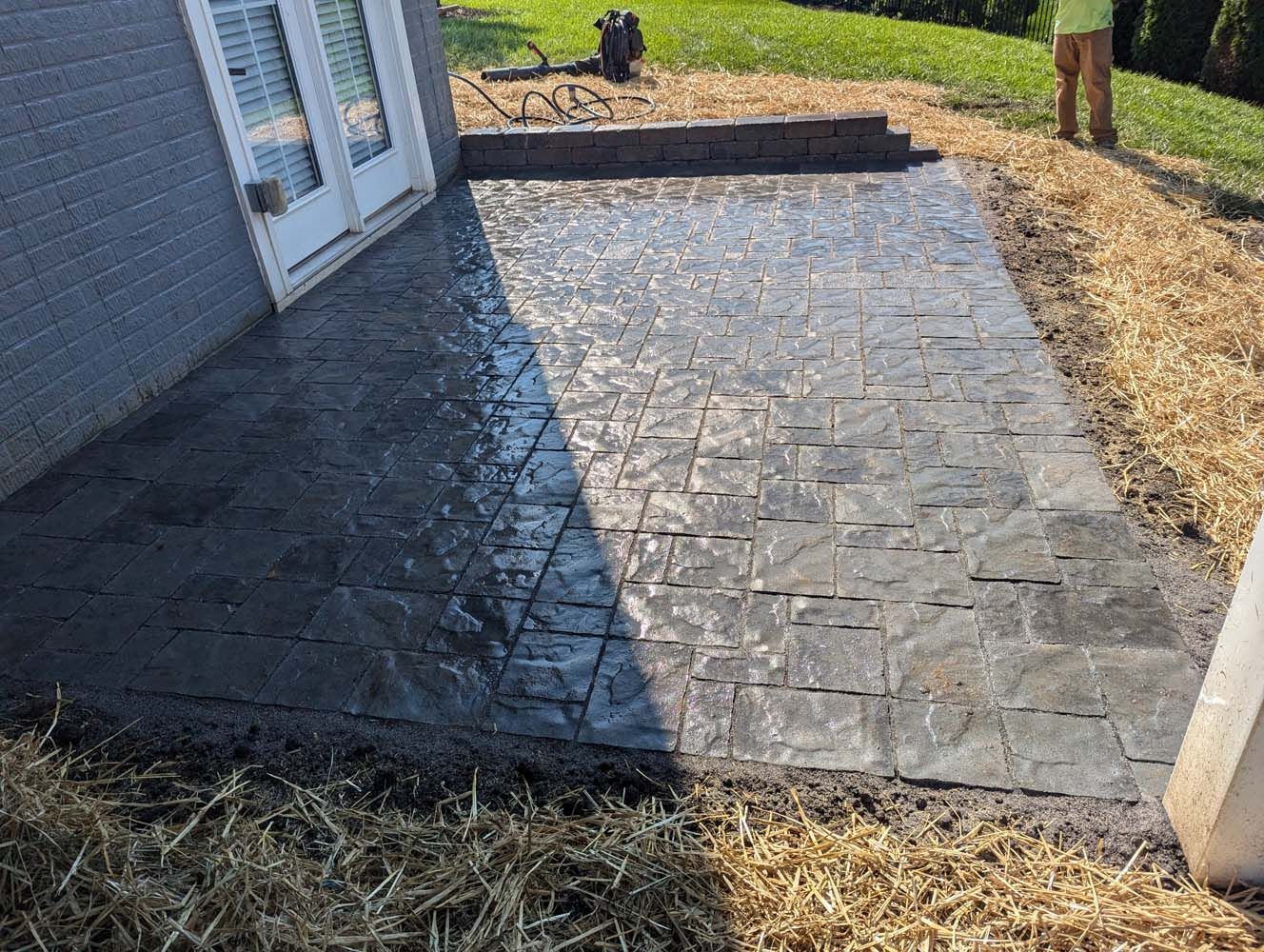 Newly constructed concrete patio with a stone pattern, next to a house and grass.