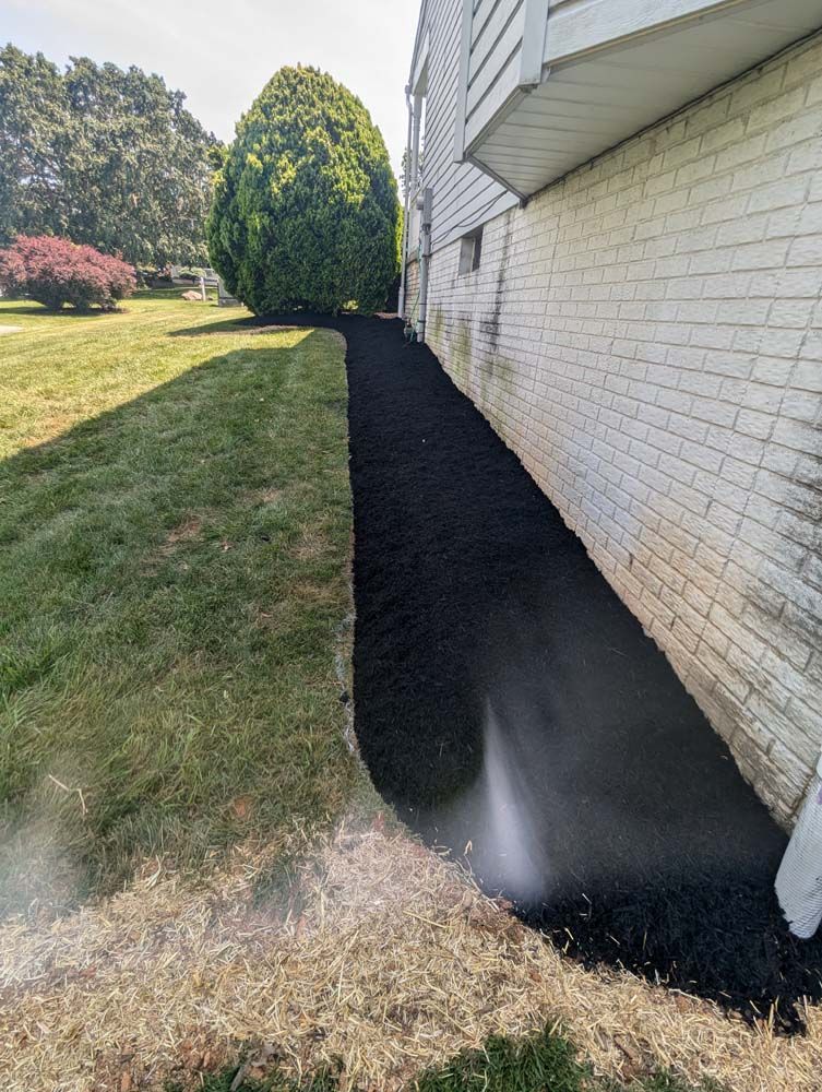 Black mulch bed alongside white brick building and green lawn; water spraying.