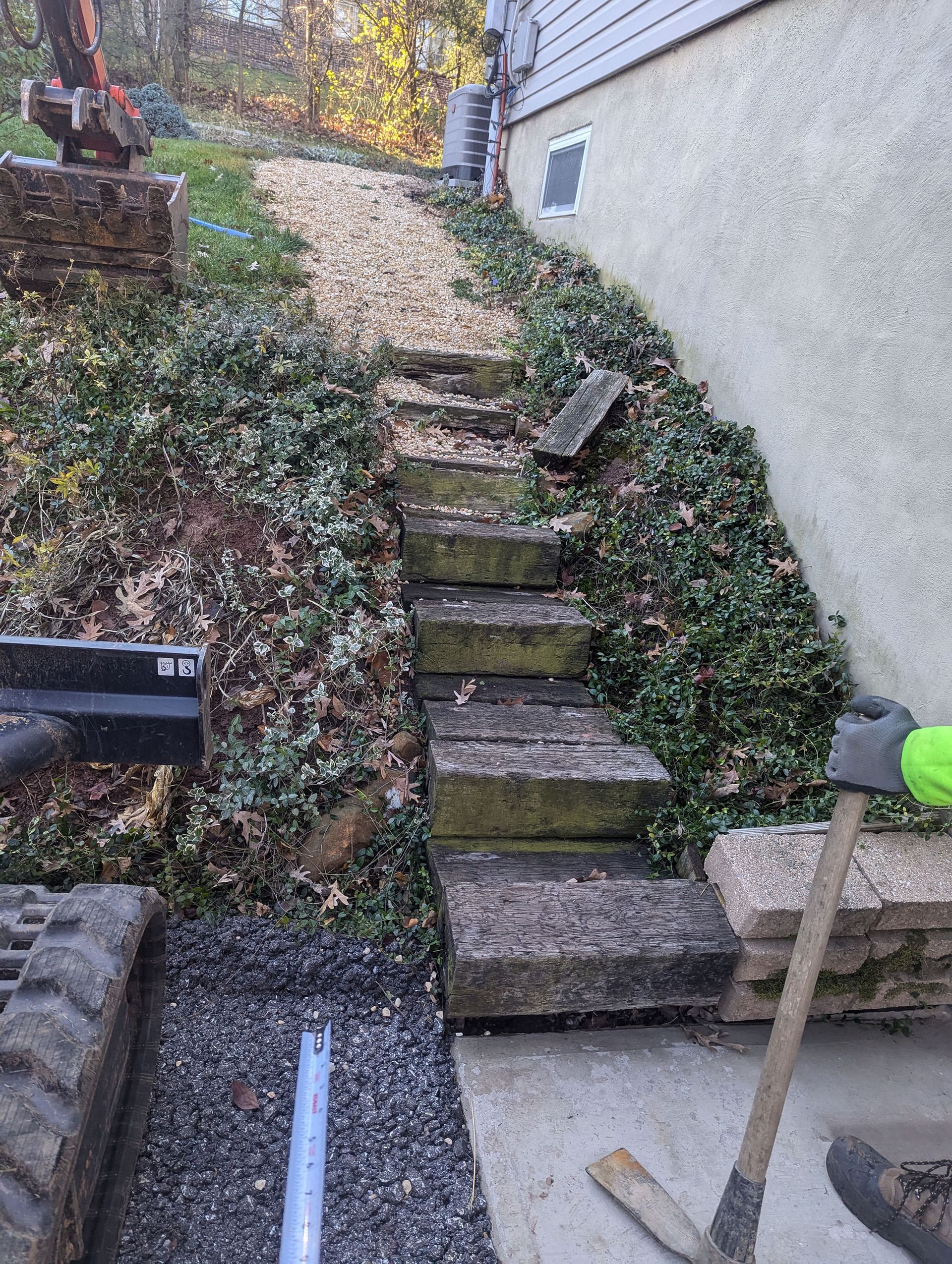 Stone steps leading up a hillside, covered in ivy. Excavator at top, next to a building.
