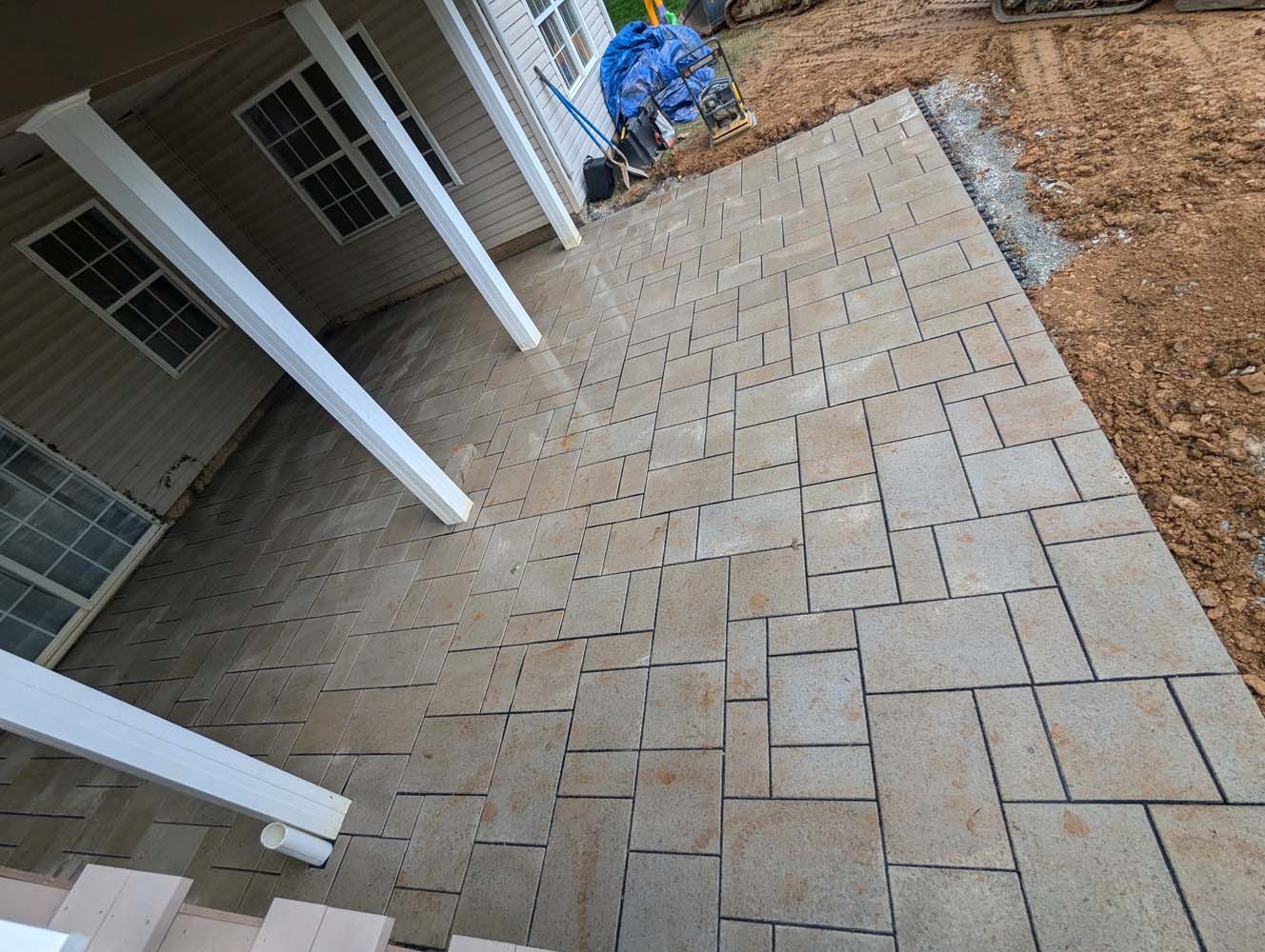 Stone patio with beige pavers extending from a covered porch with white columns.