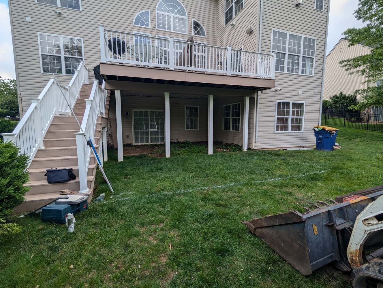 Backyard with a two-story deck, stairs, and a skid steer. The grass is green.