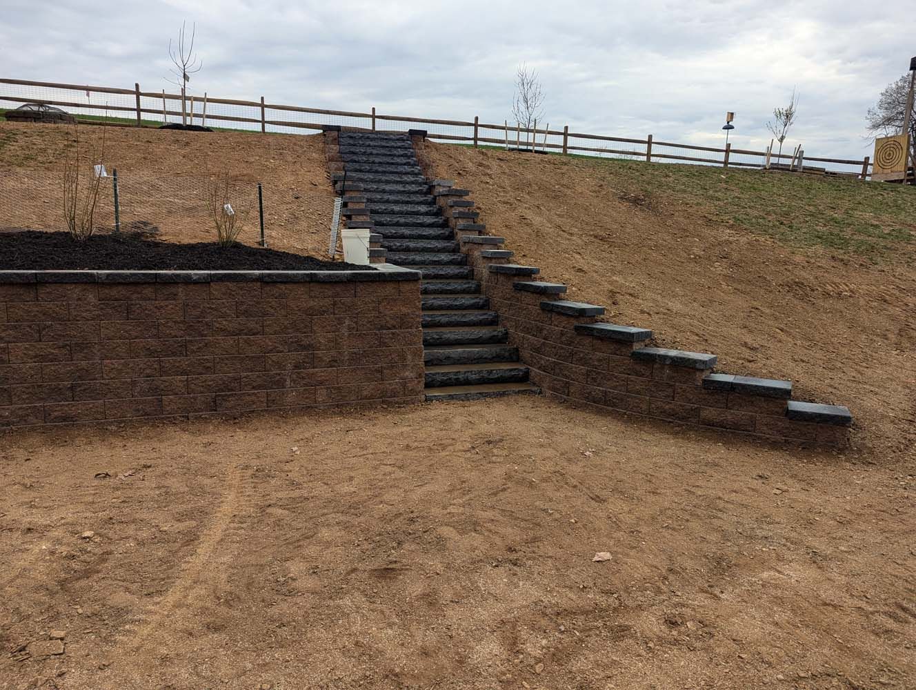 Stone steps leading up a hillside, supported by retaining walls, under a cloudy sky.