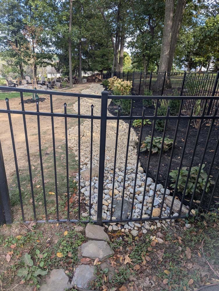 Black metal fence bordering a gravel dry creek bed in a yard with trees.