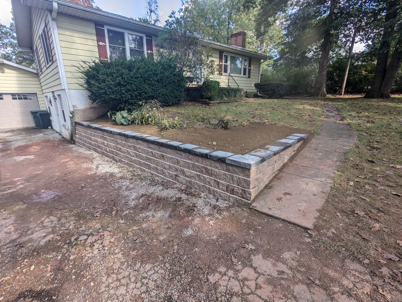 House with a newly constructed brick retaining wall bordering a flower bed and a pathway.