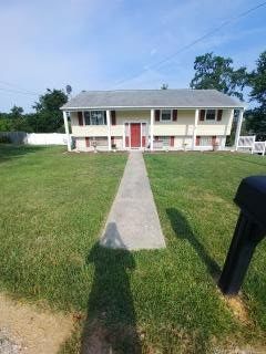 Split-level beige house with red door and trim, white pillars, and sidewalk leading to it on a sunny day.
