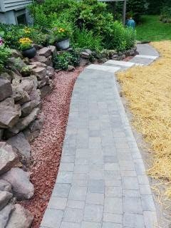 Stone walkway curves through a landscaped garden with a rock retaining wall on the left, and straw on the right.