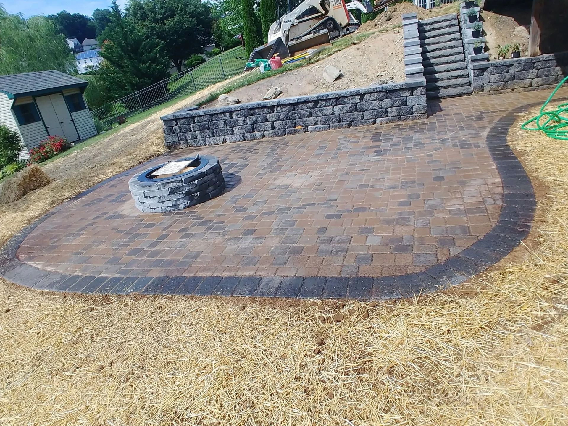 Paver patio with fire pit, retaining wall, and stairs on a sloped yard.