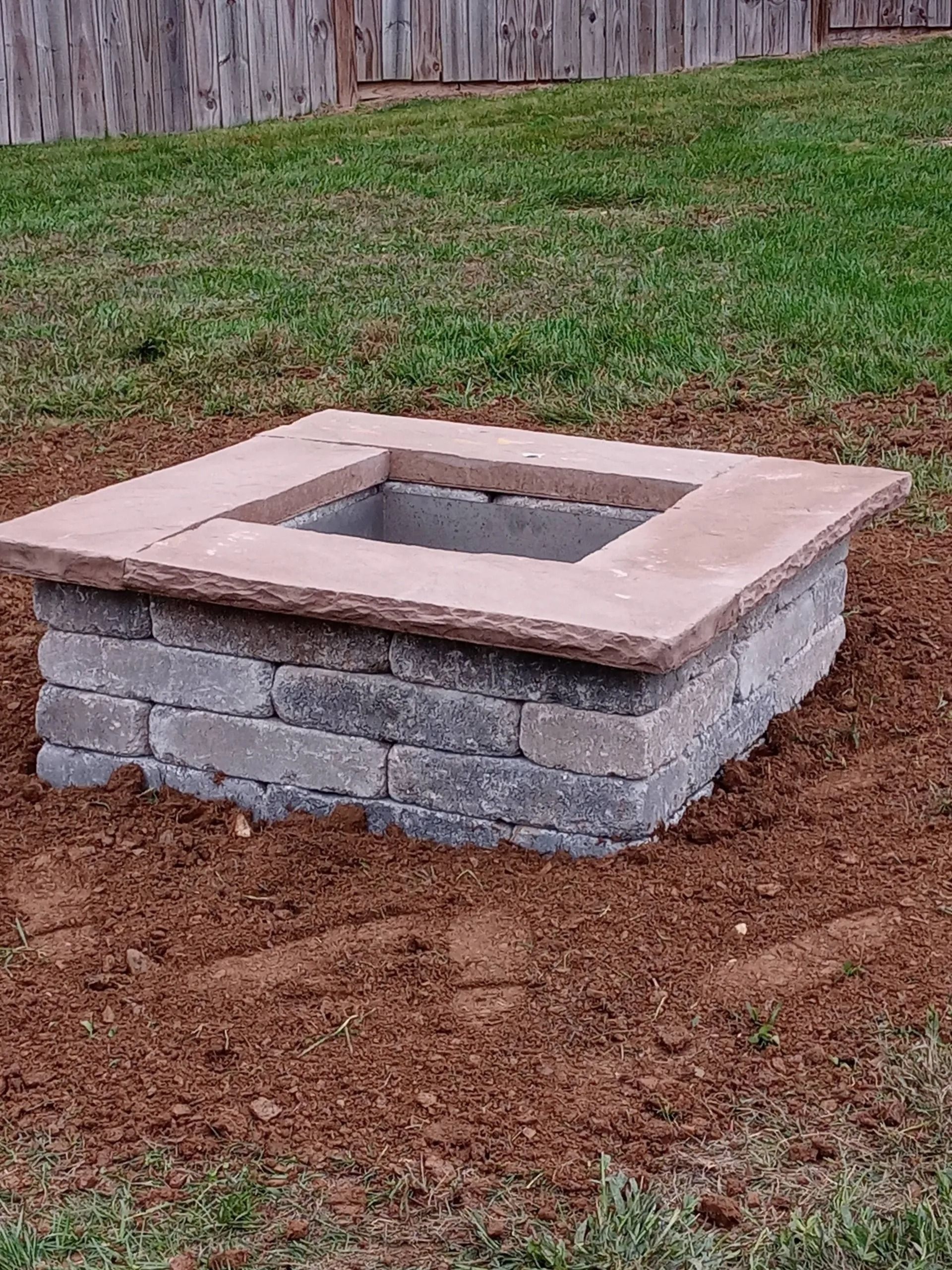 Stone fire pit in a yard with dirt and grass.