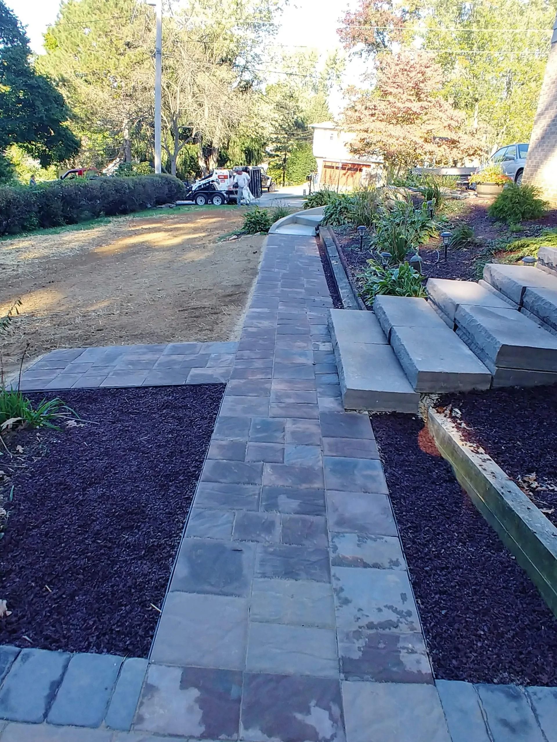 Stone walkway and steps with purple mulch and greenery, leading toward a group of people.