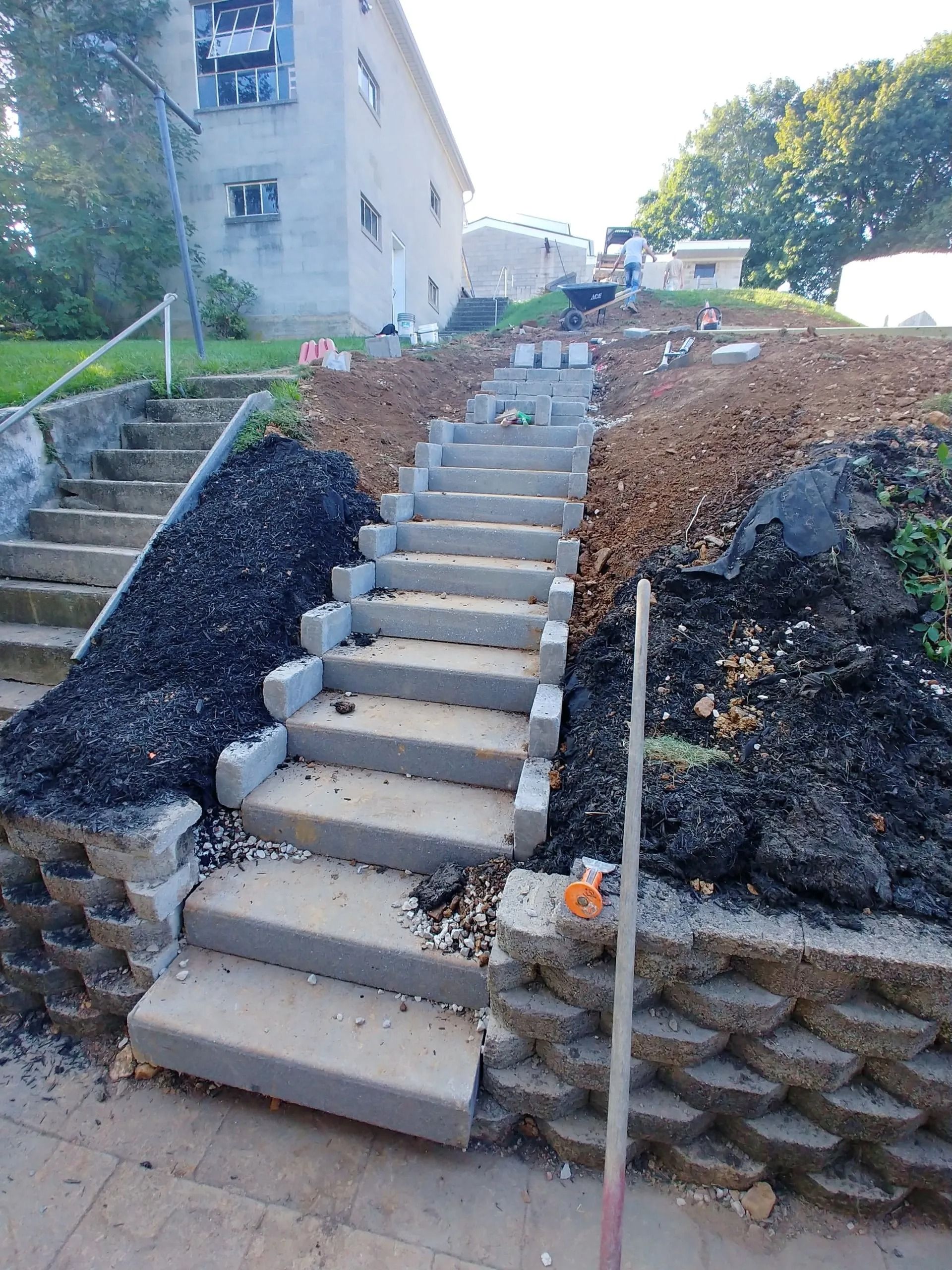 Concrete stairs being constructed on a sloped hillside, with retaining walls and surrounding dirt.