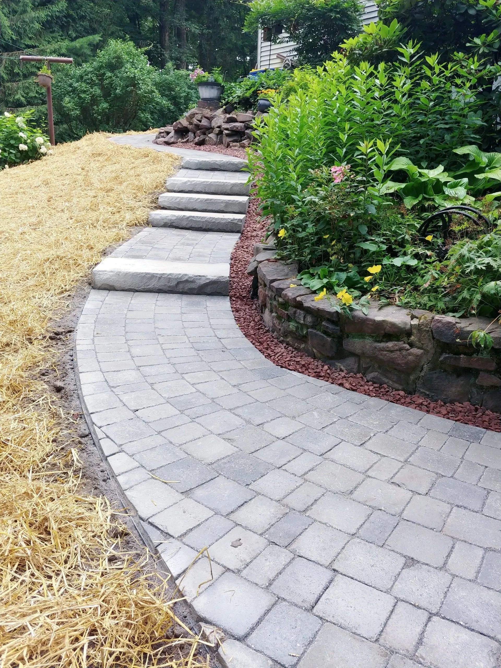 Stone walkway curving toward steps up a landscaped garden.