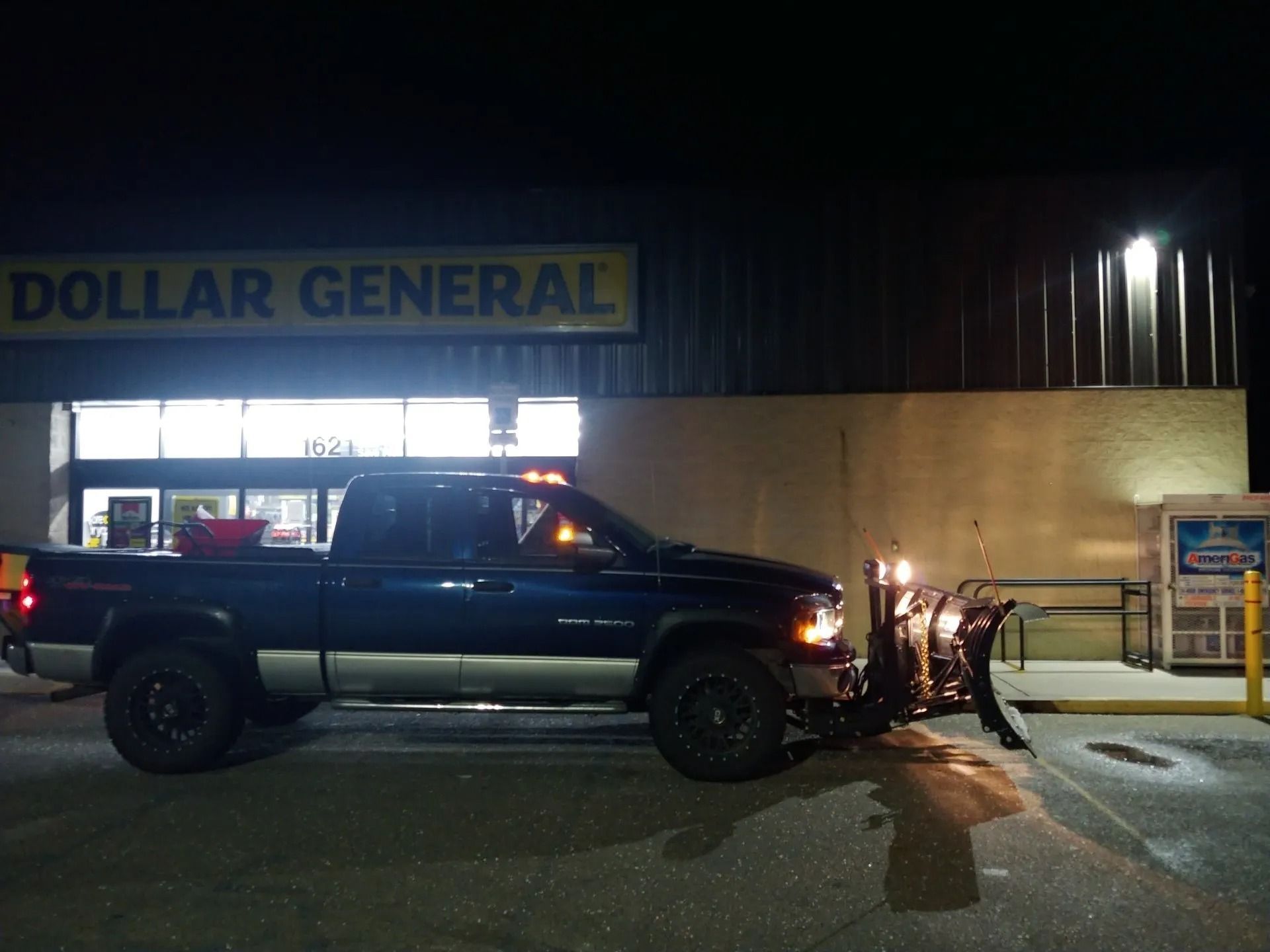 Dark blue pickup truck with snowplow parked in front of a Dollar General store at night.