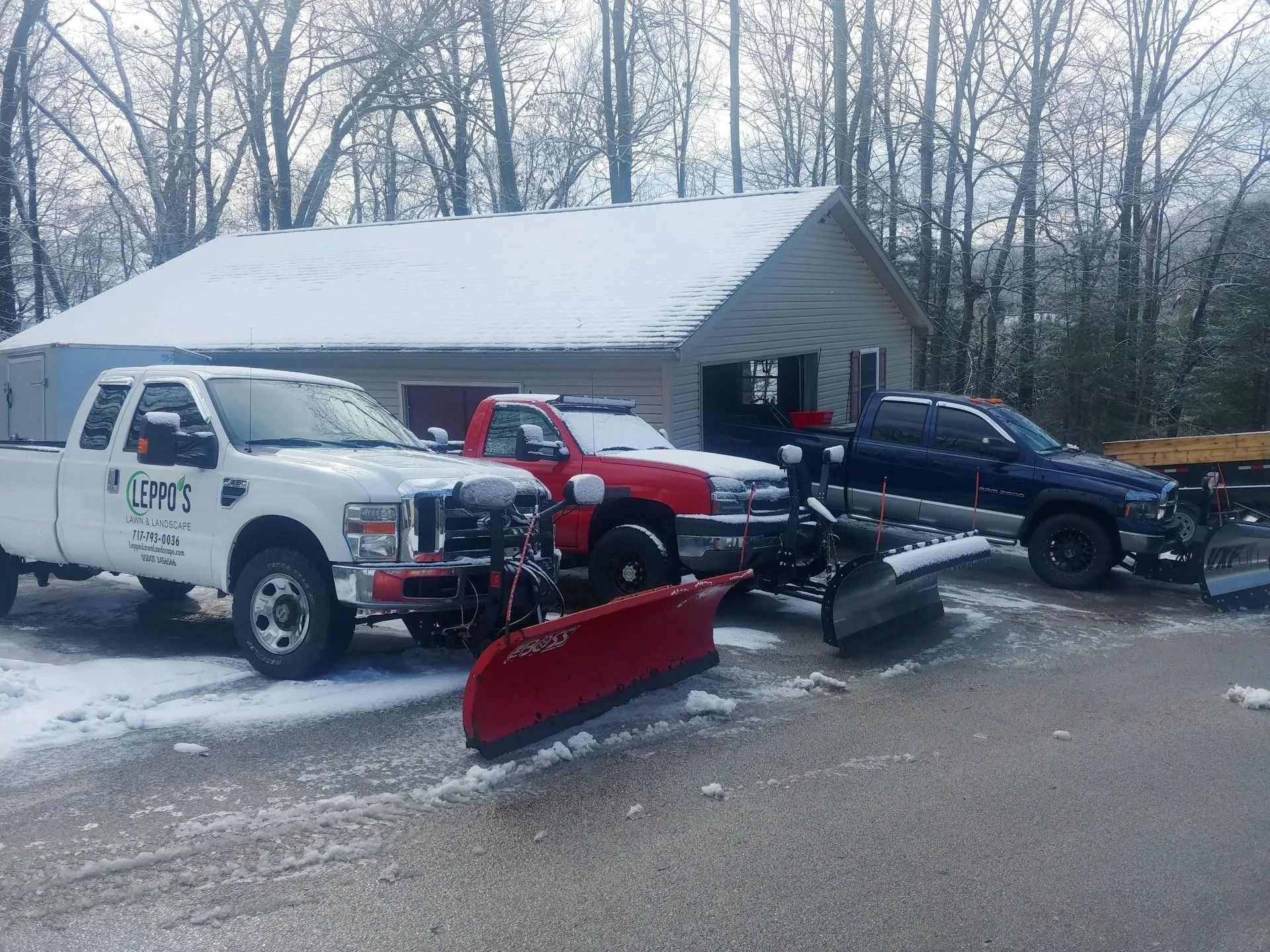 Snow-covered trucks with plows parked in front of a building, ready for snow removal.