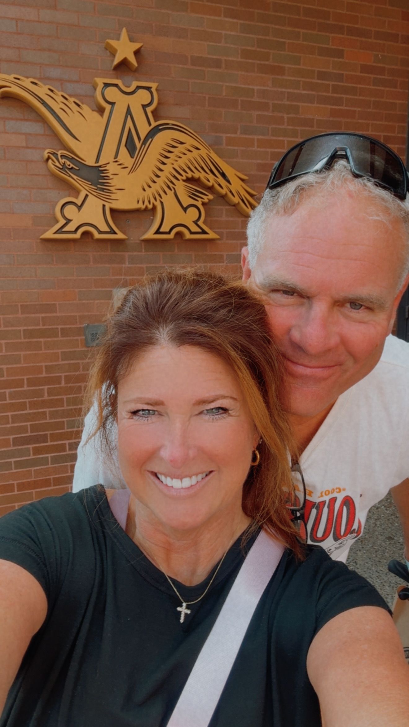 Smiling couple taking a selfie in front of a brick wall with a gold eagle emblem.