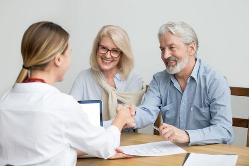 Two people shaking hands with a smiling doctor during a consultation at a desk