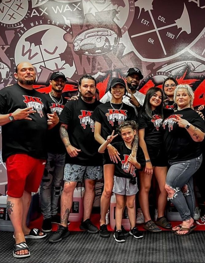 Group of people wearing matching shirts pose in front of a wall graphic.