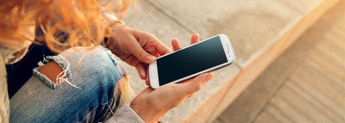 Person holding a smartphone with a blank screen, resting on a wooden surface.
