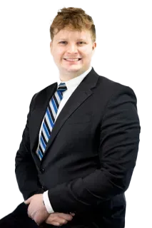 Man in a black suit with a blue and white striped tie, smiling.
