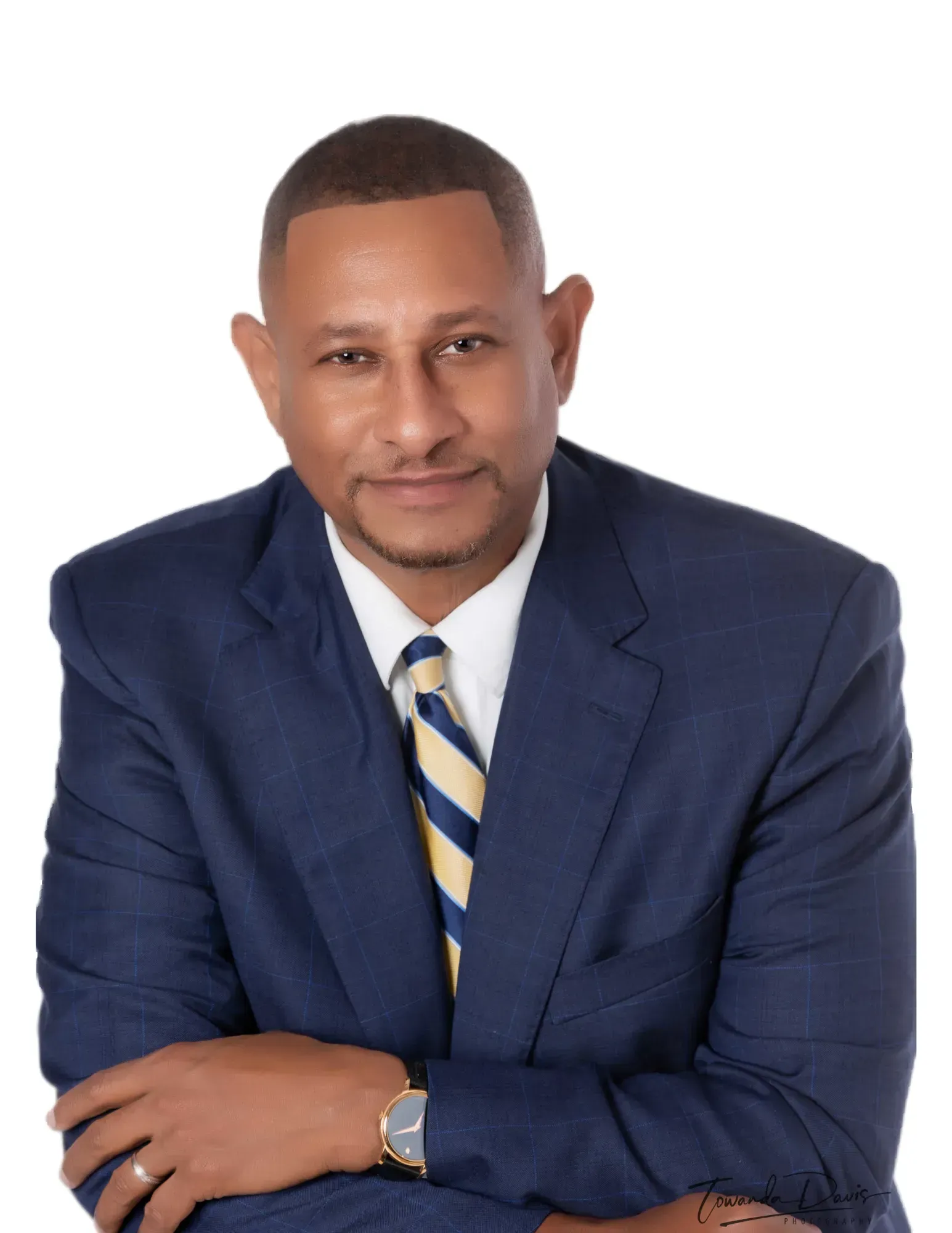 Man in blue suit, arms crossed, smiling, wearing a tie with yellow stripes.