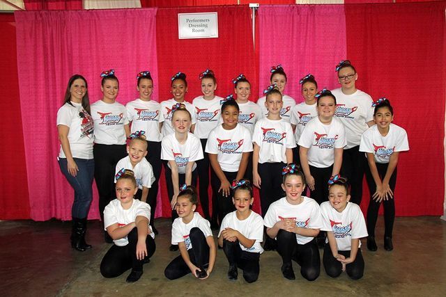 A group of young girls are posing for a picture in front of a pink curtain.