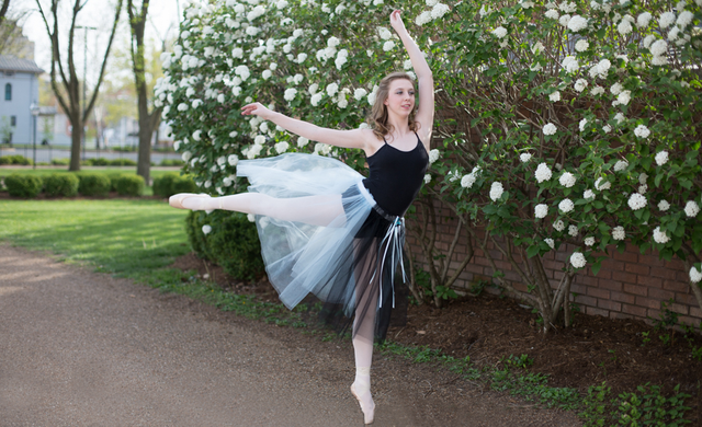 A ballerina is jumping in the air in front of a tree with white flowers.