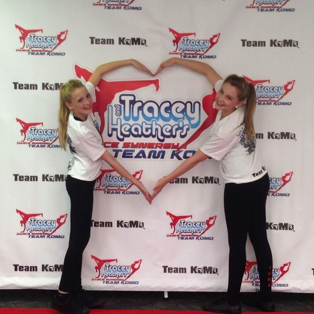 Two girls are making a heart shape with their hands in front of a tracey heather 's team logo