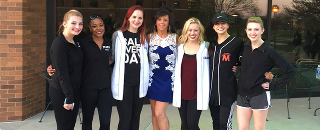 A group of young women are posing for a picture in front of a brick building.